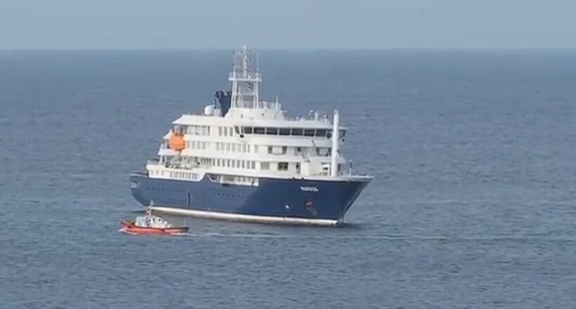 Large white and blue luxury yacht on calm open water with a small red dinghy nearby.