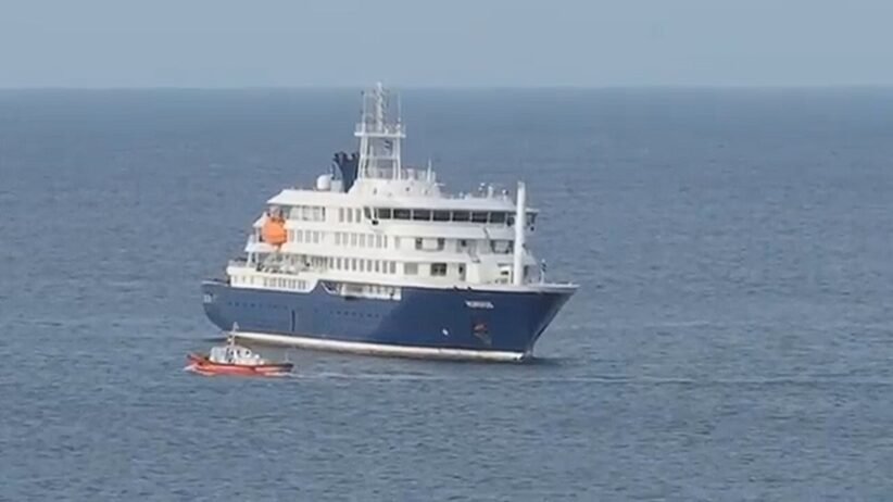 Large white and blue luxury yacht on calm open water with a small red dinghy nearby.