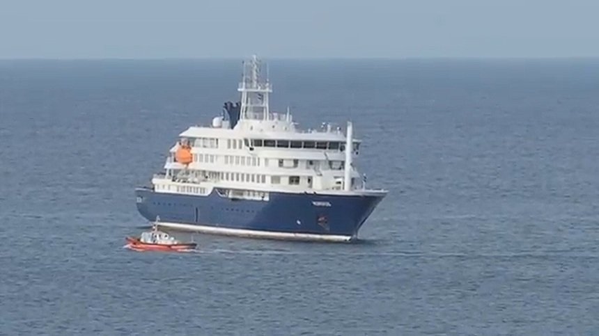 Large white and blue luxury yacht on calm open water with a small red dinghy nearby.