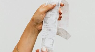 Hand holding a long, printed receipt strip between fingers with itemized text visible