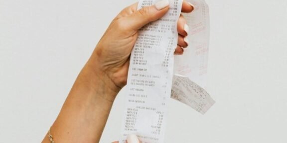 Hand holding a long, printed receipt strip between fingers with itemized text visible