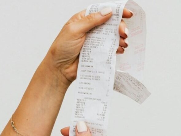 Hand holding a long, printed receipt strip between fingers with itemized text visible