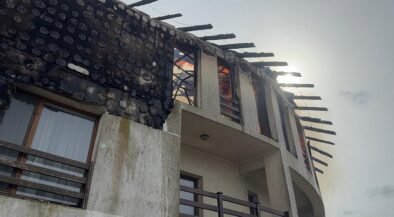 Two-story house with a severely burnt roof and exposed beams after a fire, soot on the walls you can see through the windows.