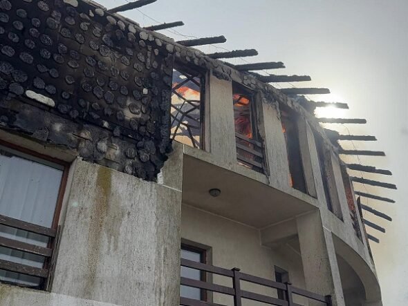 Two-story house with a severely burnt roof and exposed beams after a fire, soot on the walls you can see through the windows.