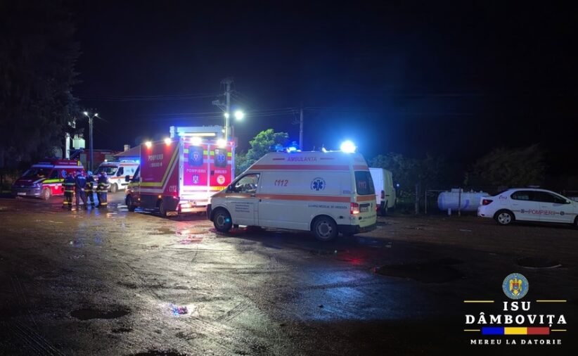 Nighttime emergency scene with ambulances and fire trucks, responders on a wet street with flashing lights.