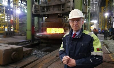 Industrial foreman in hard hat and safety jacket beside a glowing molten metal furnace in a factory.