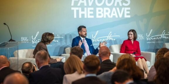 Panel discussion with three speakers on stage; backdrop reads 'Fortune Favours The Brave'.
