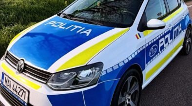 Politia police car in blue and white livery with blue and yellow stripes parked on a rural road by a yellow-field, front angled toward viewer (Romanian police).