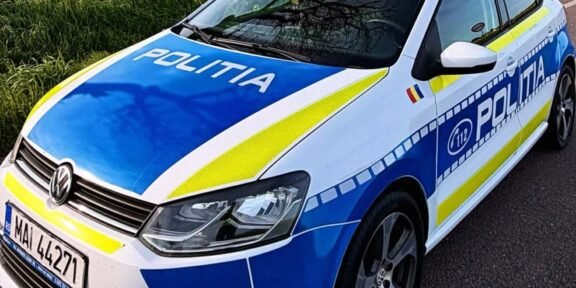 Politia police car in blue and white livery with blue and yellow stripes parked on a rural road by a yellow-field, front angled toward viewer (Romanian police).