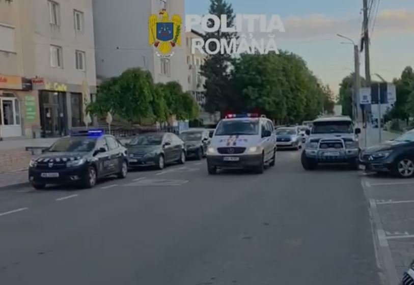 Line of Romanian police cars on a city street with a white van in front and flashing blue lights; 'Politia Romana' watermark and crest visible above.