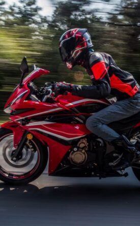 Rider in protective gear on a red sport motorcycle speeding along a road with blurred background.
