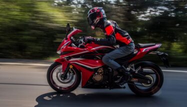 Rider in protective gear on a red sport motorcycle speeding along a road with blurred background.