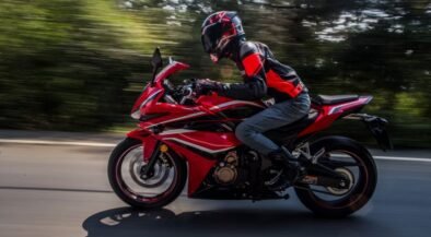 Rider in protective gear on a red sport motorcycle speeding along a road with blurred background.