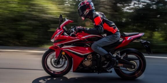 Rider in protective gear on a red sport motorcycle speeding along a road with blurred background.