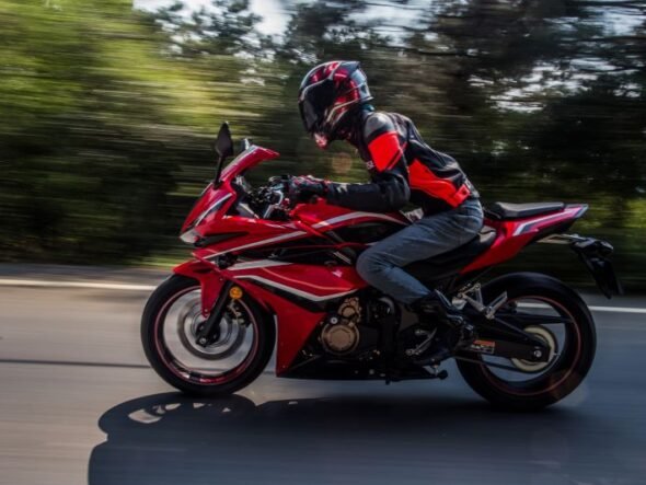 Rider in protective gear on a red sport motorcycle speeding along a road with blurred background.