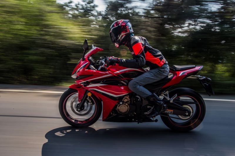 Rider in protective gear on a red sport motorcycle speeding along a road with blurred background.