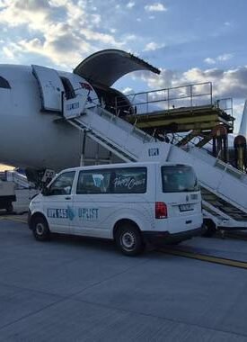 Commercial airplane parked on the tarmac with mobile boarding stairs connected to the door and a white service van beside it at sunset.