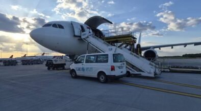 Commercial airplane parked on the tarmac with mobile boarding stairs connected to the door and a white service van beside it at sunset.