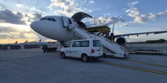 Commercial airplane parked on the tarmac with mobile boarding stairs connected to the door and a white service van beside it at sunset.