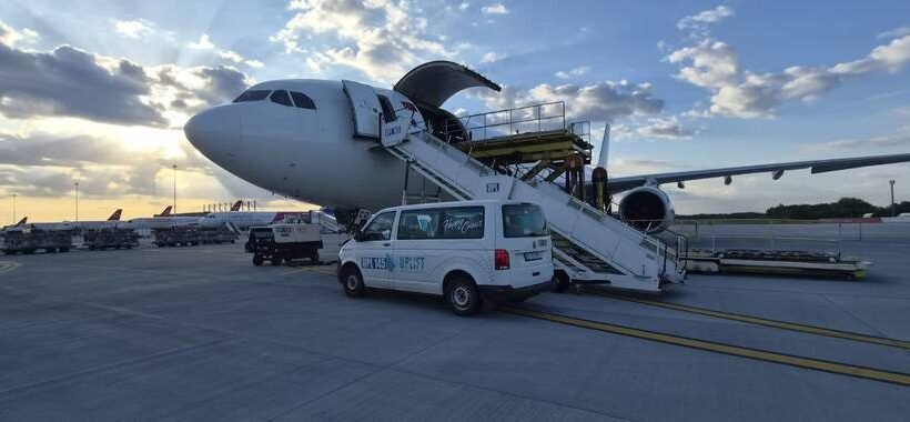 Commercial airplane parked on the tarmac with mobile boarding stairs connected to the door and a white service van beside it at sunset.