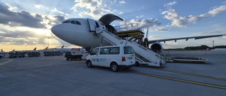 Commercial airplane parked on the tarmac with mobile boarding stairs connected to the door and a white service van beside it at sunset.