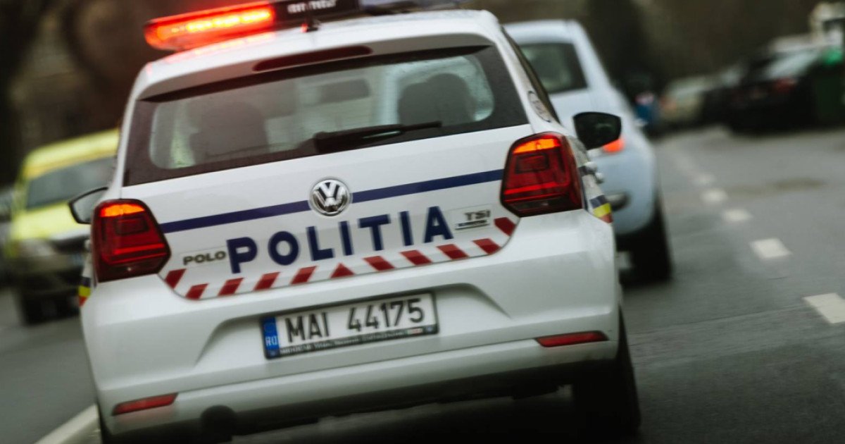 Rear view of a white Romanian police car with 'POLITIA' on the trunk and red emergency lights flashing on the roof, driving on a street.