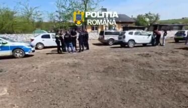 Group of police officers and civilians gathered near parked cars on a dirt lot in a rural area; Romanian police car visible.