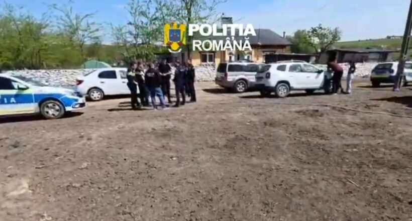 Group of police officers and civilians gathered near parked cars on a dirt lot in a rural area; Romanian police car visible.