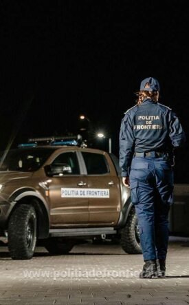 Two border police officers in uniform walk away from a patrol pickup at night, a 'Politia de Frontiera' vehicle nearby.