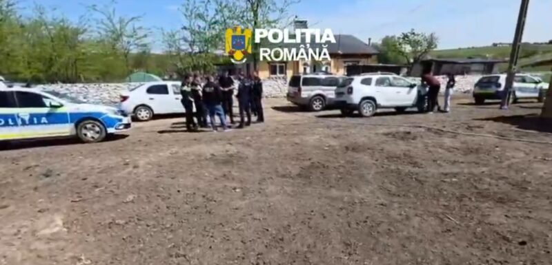 Group of police officers and civilians gathered near parked cars on a dirt lot in a rural area; Romanian police car visible.