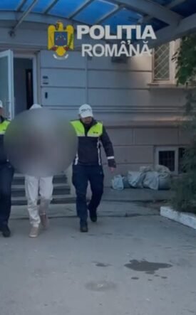 Two Romanian police officers escort a detainee with face blurred outside a building marked Politia Romana.