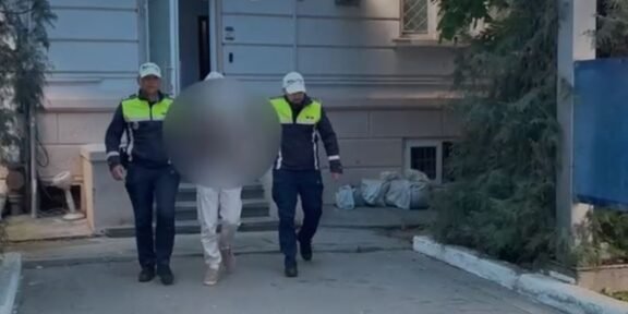 Two Romanian police officers escort a detainee with face blurred outside a building marked Politia Romana.
