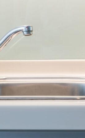 Chrome kitchen faucet over a stainless steel kitchen sink, close-up view on the left side of the basin.
