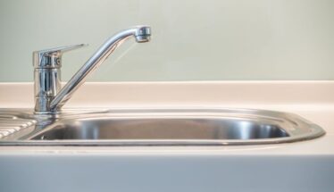 Chrome kitchen faucet over a stainless steel kitchen sink, close-up view on the left side of the basin.