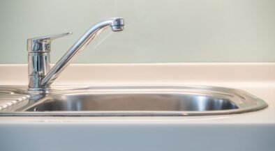 Chrome kitchen faucet over a stainless steel kitchen sink, close-up view on the left side of the basin.