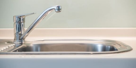 Chrome kitchen faucet over a stainless steel kitchen sink, close-up view on the left side of the basin.