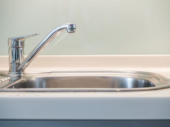 Chrome kitchen faucet over a stainless steel kitchen sink, close-up view on the left side of the basin.