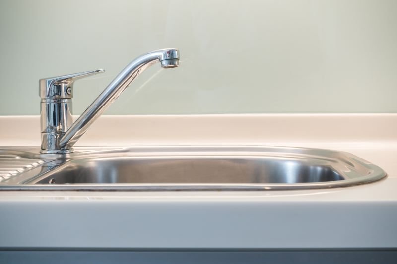 Chrome kitchen faucet over a stainless steel kitchen sink, close-up view on the left side of the basin.