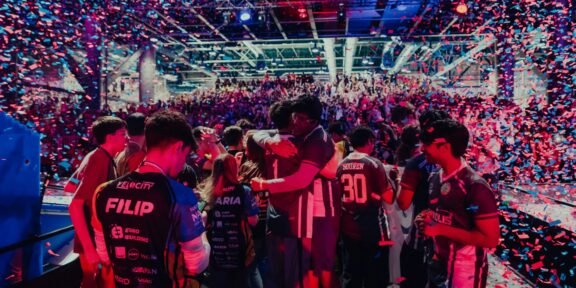 Crowded esports arena celebrating on stage with colorful confetti showering over players and fans.