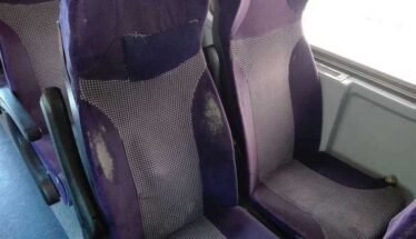 Purple upholstered bus seats with visible wear, scuffs, and stains on the fabric shapes in a row of seats