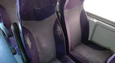 Purple upholstered bus seats with visible wear, scuffs, and stains on the fabric shapes in a row of seats