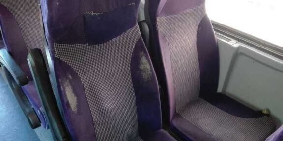 Purple upholstered bus seats with visible wear, scuffs, and stains on the fabric shapes in a row of seats