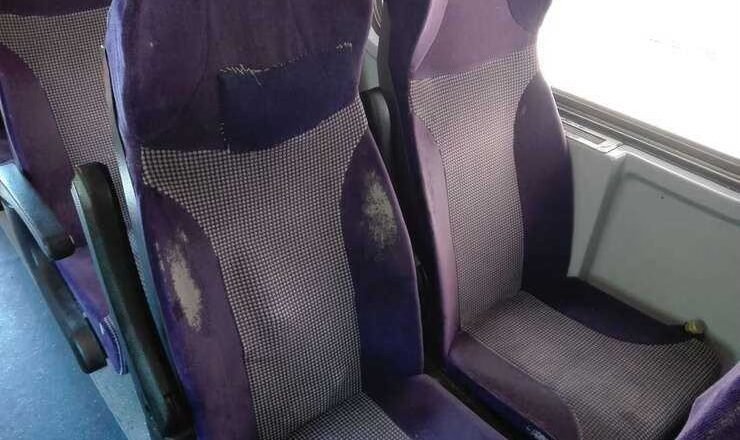 Purple upholstered bus seats with visible wear, scuffs, and stains on the fabric shapes in a row of seats