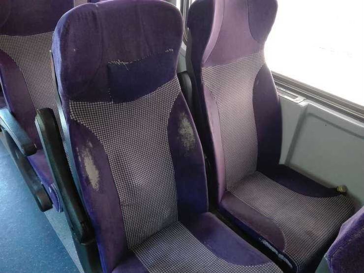 Purple upholstered bus seats with visible wear, scuffs, and stains on the fabric shapes in a row of seats