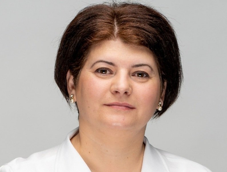 Professional head-and-shoulders portrait of a woman with short dark hair, pearl earrings, and a light gray background.