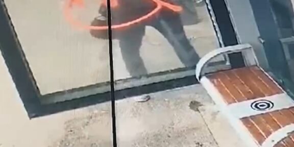 Person outside a glass storefront, seen through the window, with an orange curved mark on the glass surface.