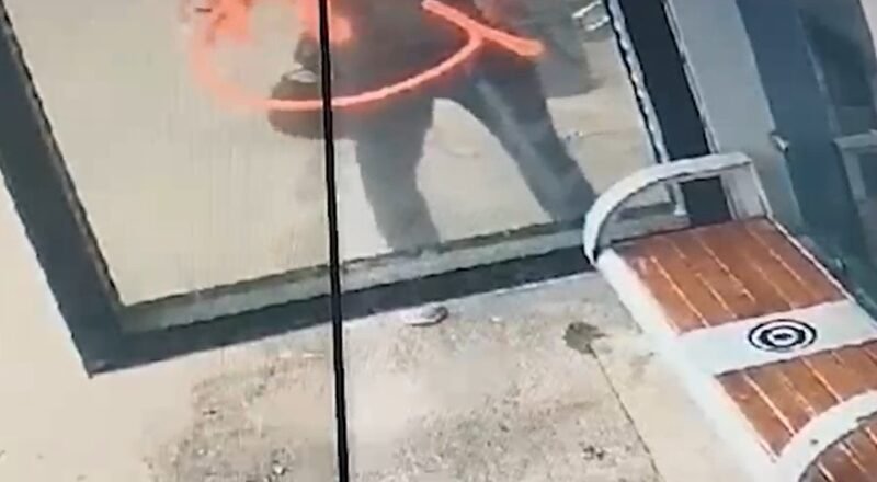 Person outside a glass storefront, seen through the window, with an orange curved mark on the glass surface.