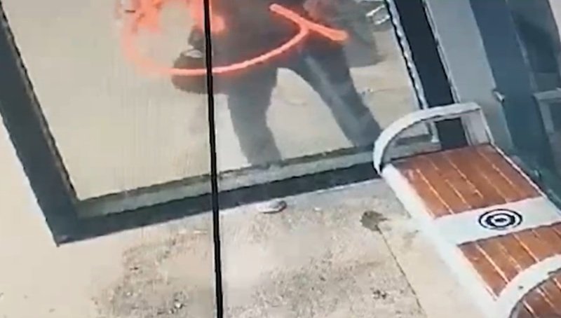 Person outside a glass storefront, seen through the window, with an orange curved mark on the glass surface.