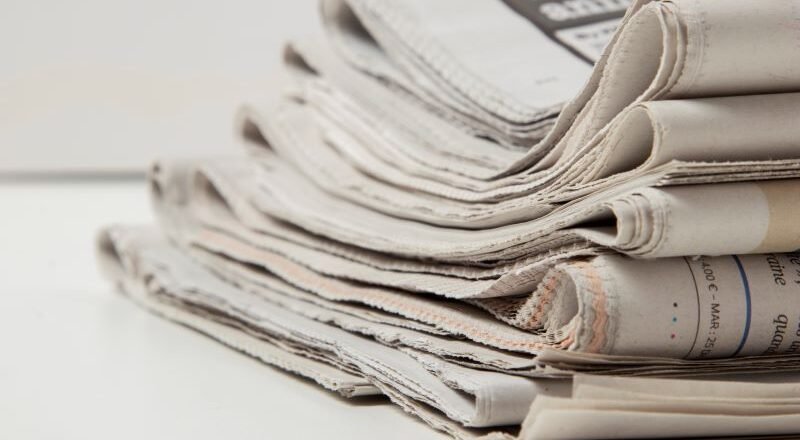 Pile of folded newspapers stacked on a white surface