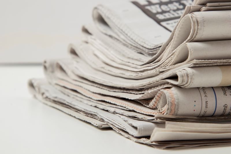 Pile of folded newspapers stacked on a white surface
